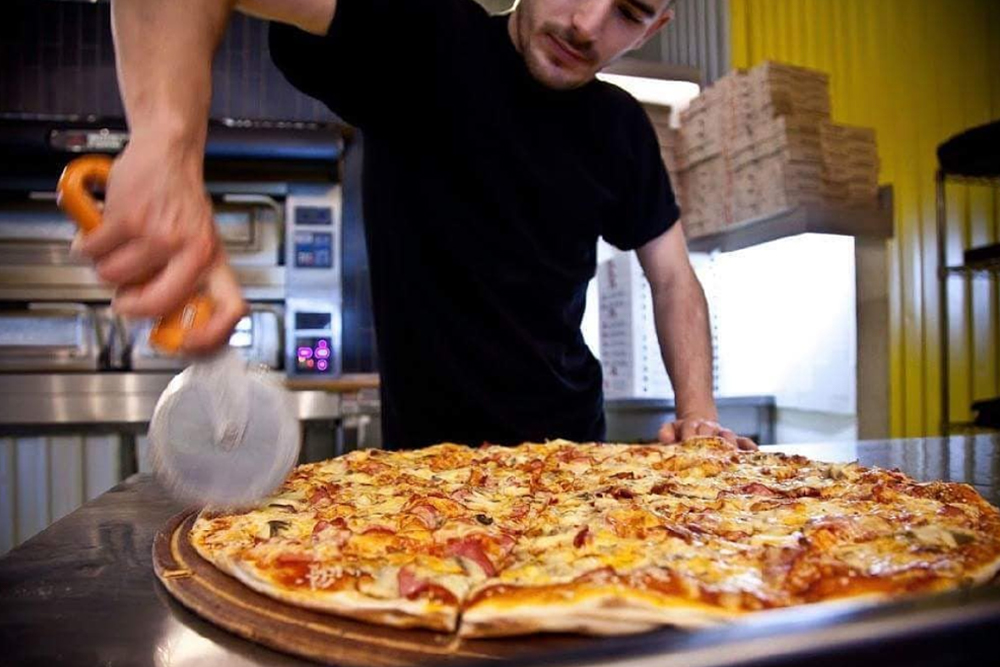 Man cutting a large gourmet pizza at Proper Pizza
