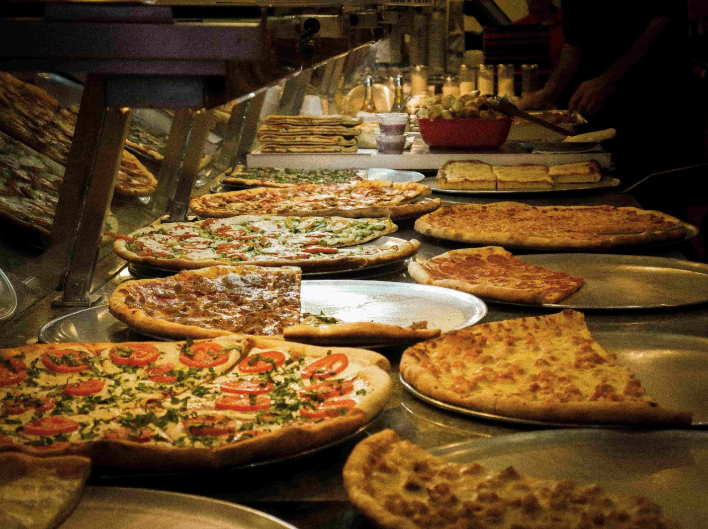 A restaurant counter with different types of pizza on it.